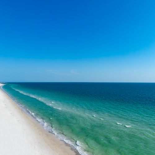 A tranquil beach scene with clear blue skies, turquoise waters, and a long stretch of sandy shoreline.