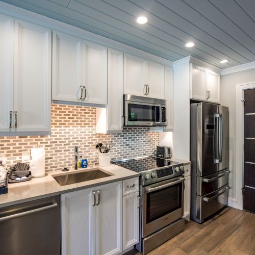 Modern kitchen with white cabinets, stainless steel appliances, tiled backsplash, sink, and coffee maker on a countertop, wood flooring.