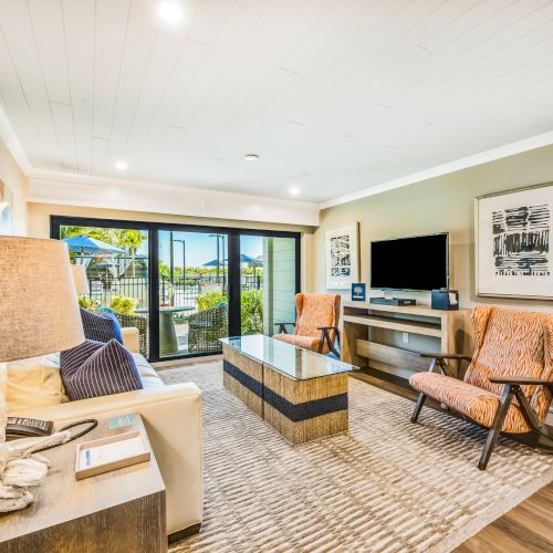 A modern living room featuring a large window, sofa, two armchairs, TV, coffee table, and decor with a view of an outdoor area with greenery.