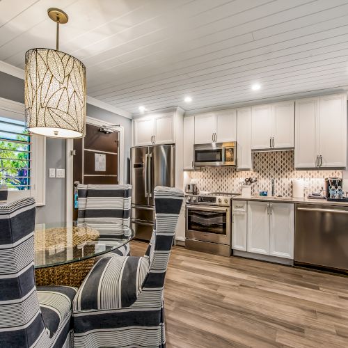 A modern kitchen and dining area with striped chairs, pendant lighting, and stainless steel appliances in a cozy, well-lit space.