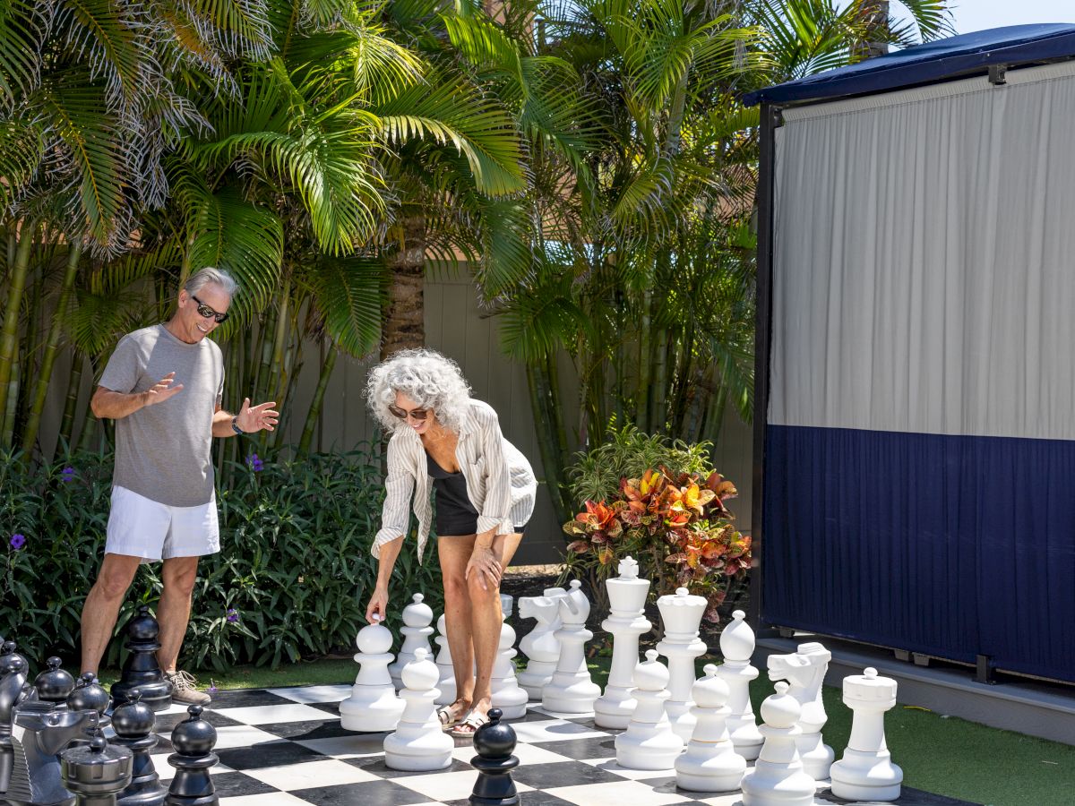 Two people are playing with large chess pieces on an outdoor chessboard.