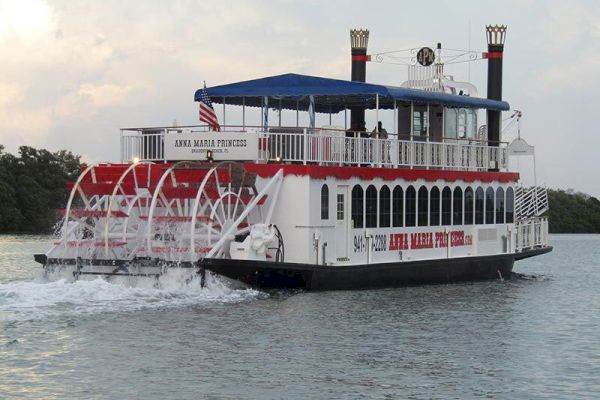 A paddle steamer boat, identified as the Anna Maria Princess, is sailing on water with trees in the background.