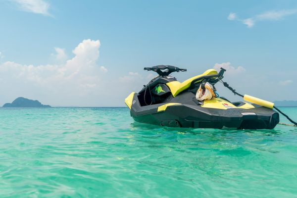 A jet ski floats on clear, turquoise water under a partly cloudy sky, with a distant island visible on the horizon.